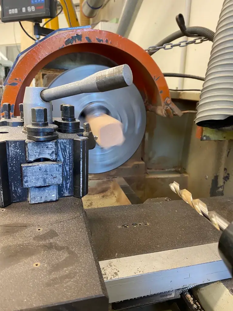 A close-up view of a woodworking machine with a sanding disc and drill bit, used during the fabrication stage.