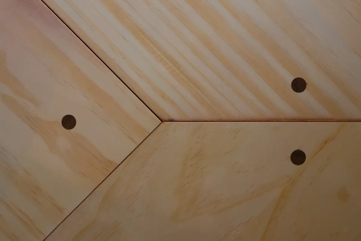 Close-up view of the plywood corner desk surface showing visible circular mounting holes.