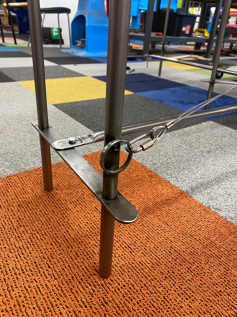 Close-up view of a steel bracket and cable attachment on a metal desk prototype.