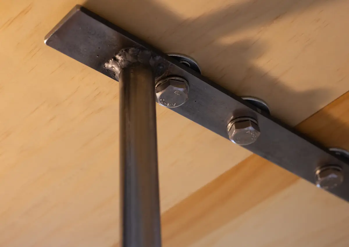 A close-up view of a raw steel bracket fastened to plywood using visible bolts.