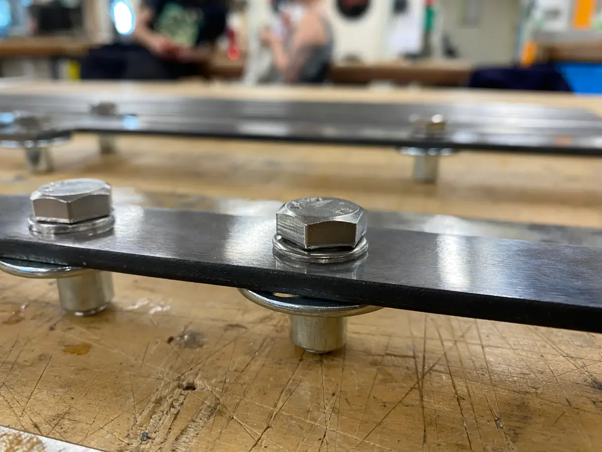 A fabricated steel support piece with visible bolts resting on a wooden workbench.