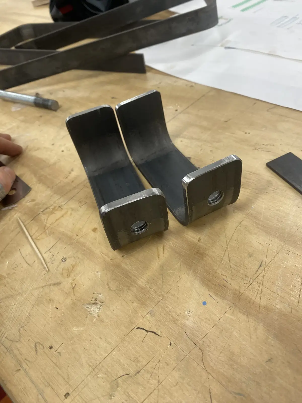 Two fabricated metal brackets with holes for screws, shown on a workbench.