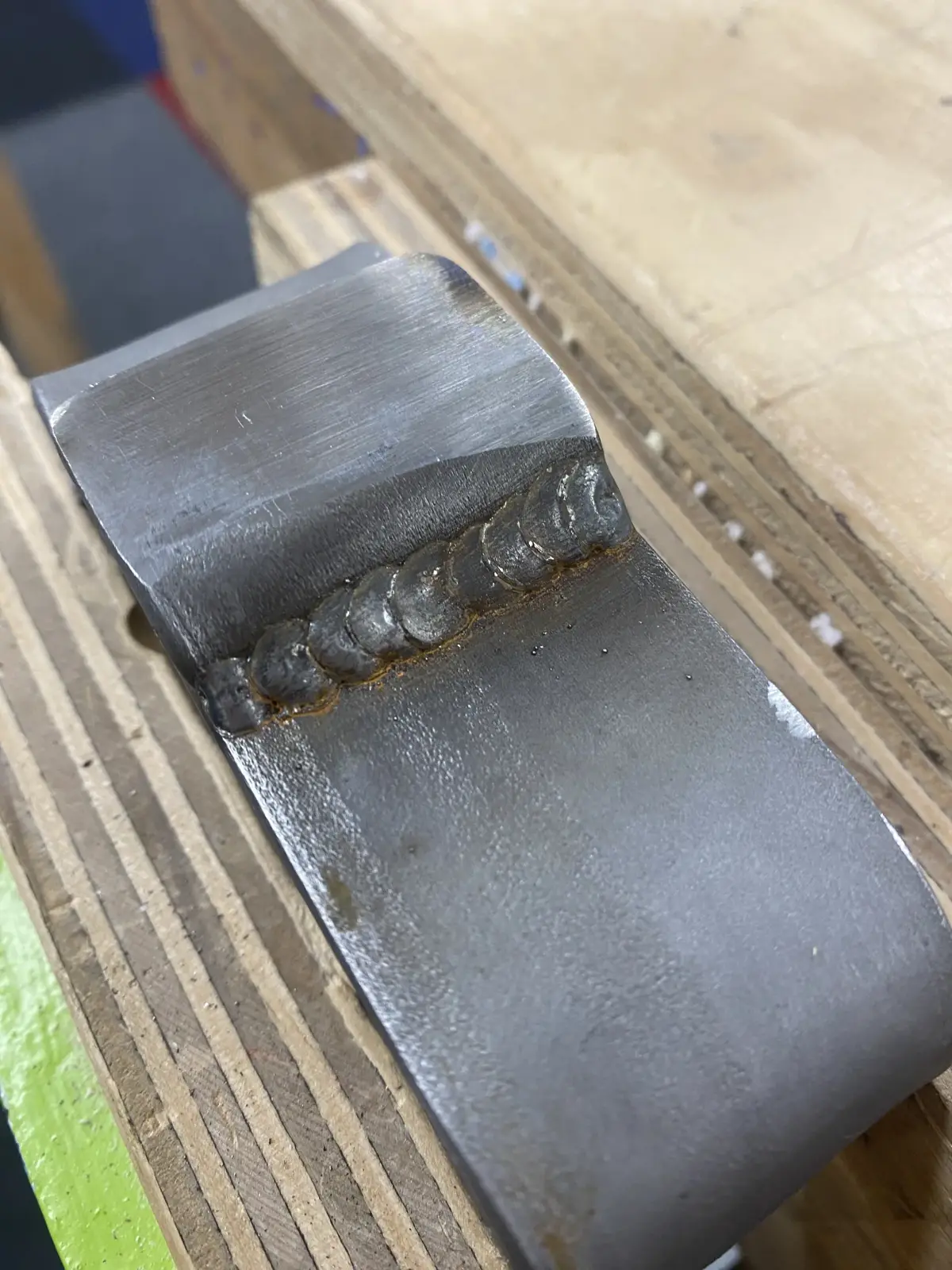 Close-up view of the fabricated metal composting tool showing a threaded section on a wooden bench.