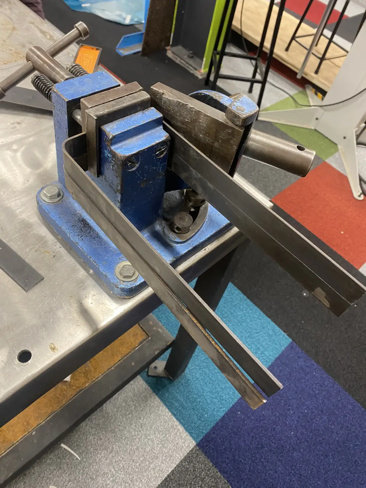 A blue metal jig and two metal bars are shown on a workbench, used for the 'Scrappy' composting project.