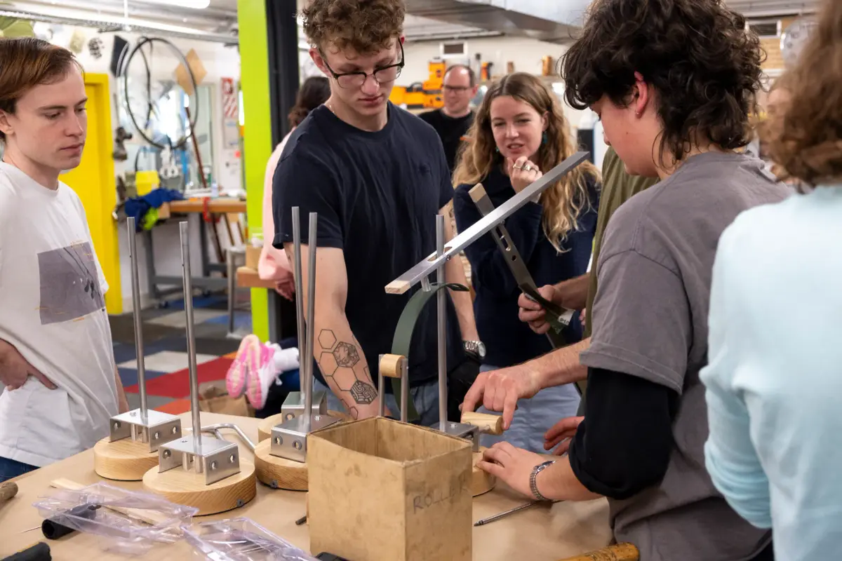 Students examine a metal and wood prototype of the 'Tei' lamp during a design review session.