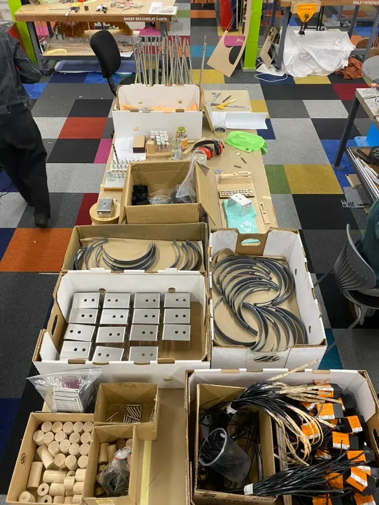 Various components, wood pieces, and metal wiring for the batch-produced Tei lamp are organized in open boxes.