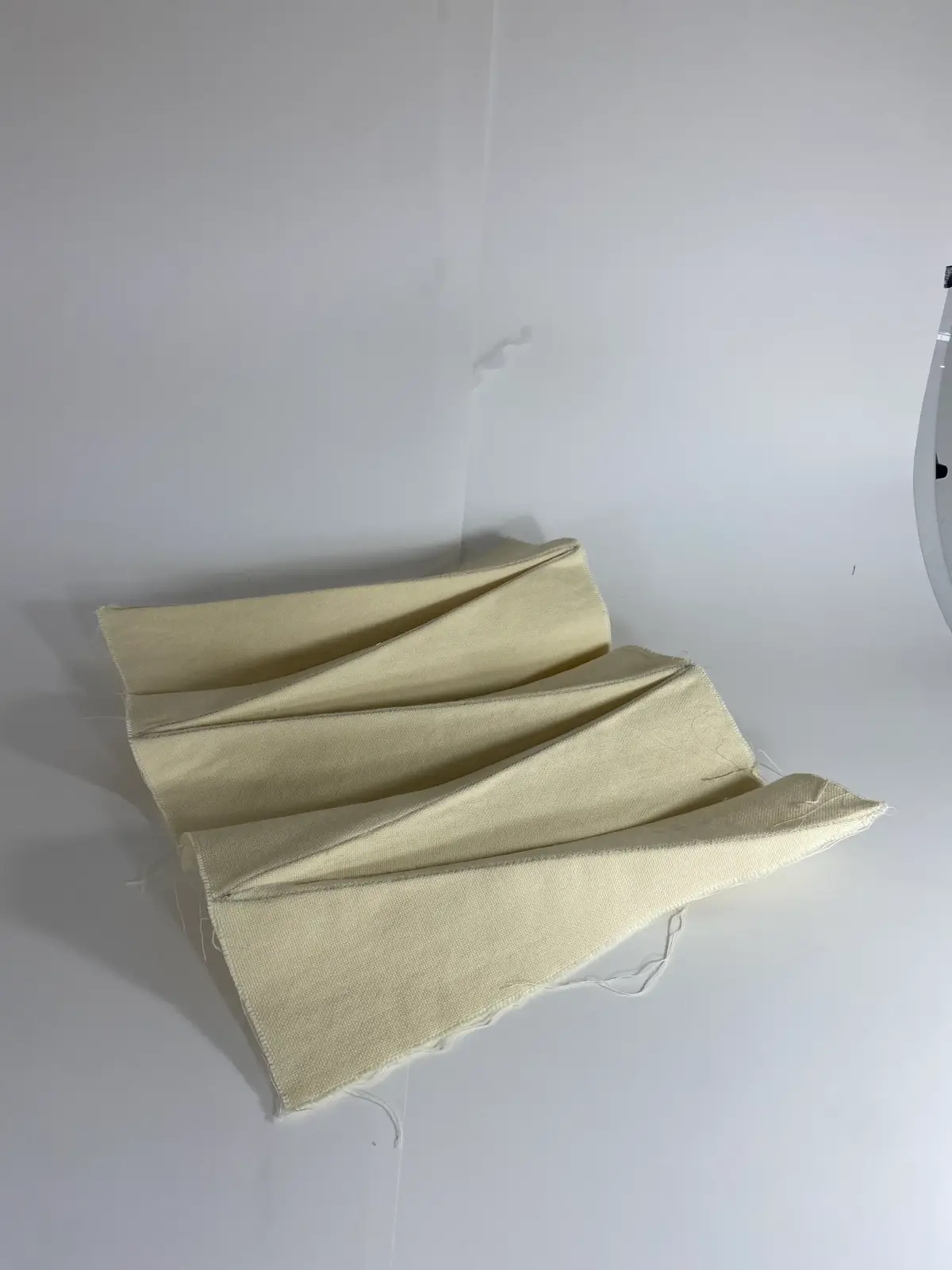 A light beige, folded textile prototype piece displayed on a plain white background.