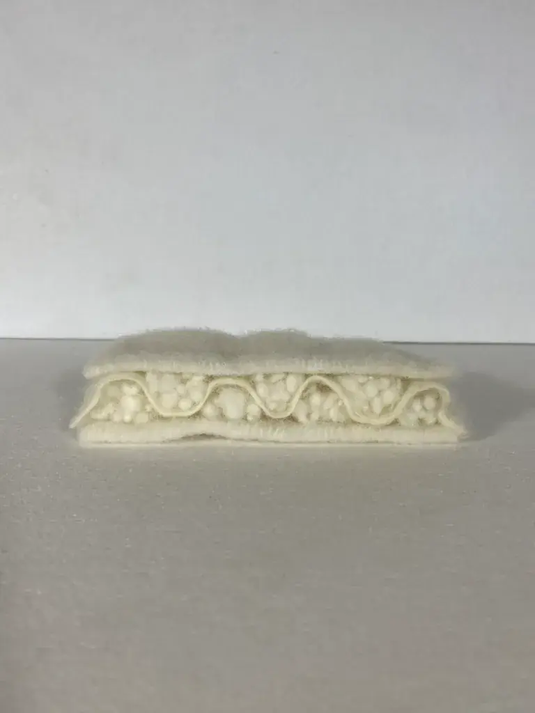 A white, knitted textile prototype featuring an embossed floral pattern, shown in a studio setting.