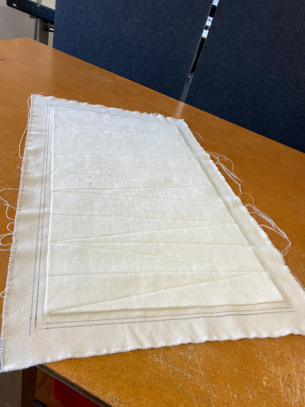 A rectangular, unbleached textile sample with visible stitching lines placed on a wooden table.
