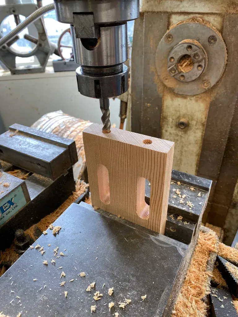 A wooden block being routed by a drill press during the fabrication stage of the project.