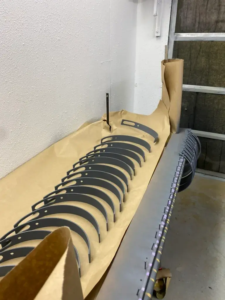 A collection of curved metal lamp parts are arranged on a sheet of cardboard next to the finished product.