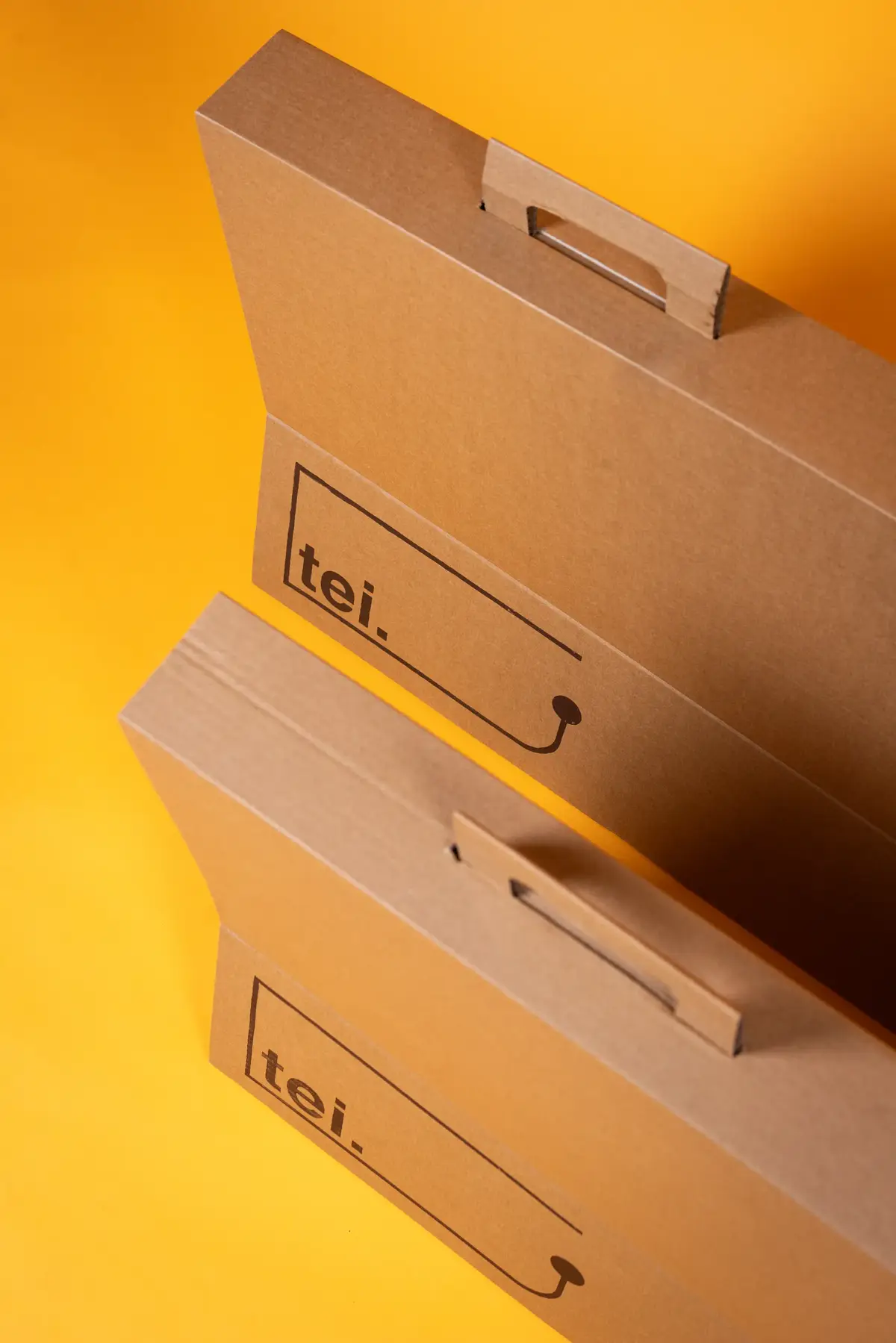 Two open, unbranded cardboard boxes showing the 'tei.' logo on a yellow background.