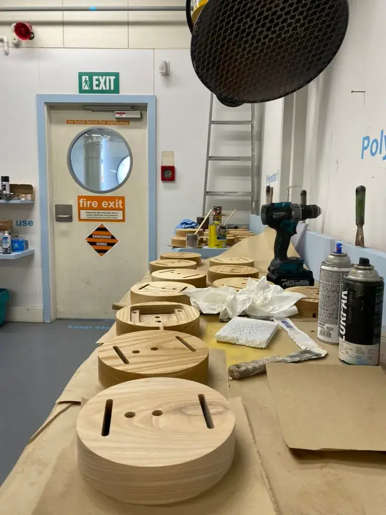 Multiple stacked wooden bases for the 'Tei' lamp prototype are visible on a covered workbench.